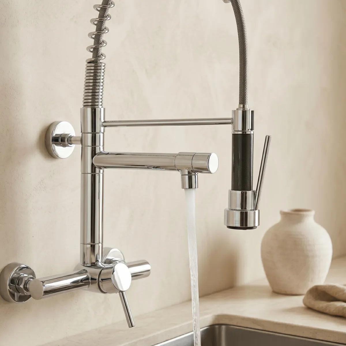 Detalhe da torneira gourmet cromada com mola e ducha flexível articulada com água em jato sobre pia de inox em cozinha minimalista