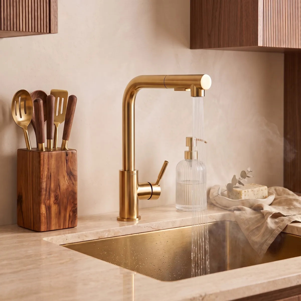 Torneira gourmet dourada extensível com bica angular e água em jato sobre pia dourada em cozinha com utensílios de madeira e ouro