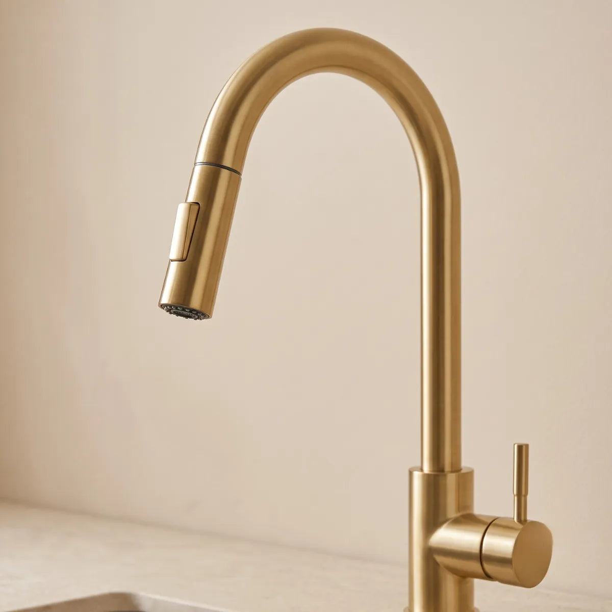 Vista aproximada da bica em arco e ducha retrátil da torneira para cozinha dourada escovada Épure, com botão seletor de jato e acabamento champagne fosco, fundo neutro.